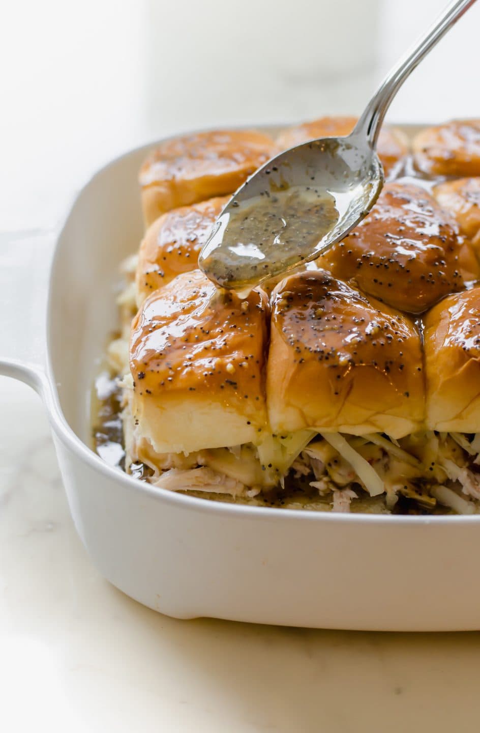 A spoon spreading the poppy seed butter sauce on top of Kentucky Hot Brown Sliders