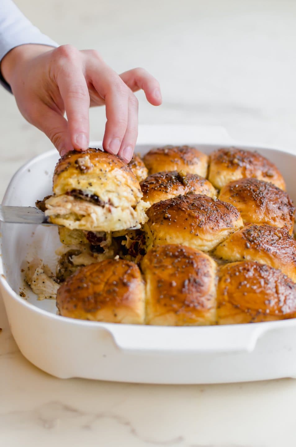 A hand lifting a Kentucky Hot Brown Slider from a baking dish.