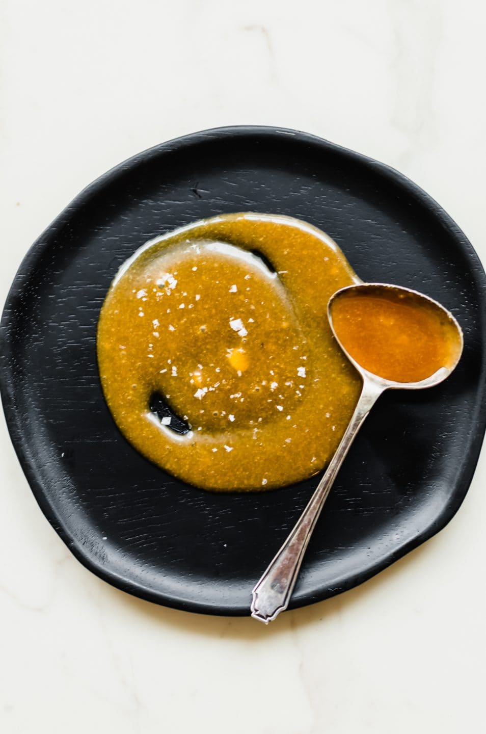 A black plate with swirls of salted caramel on it and a spoon on the side.