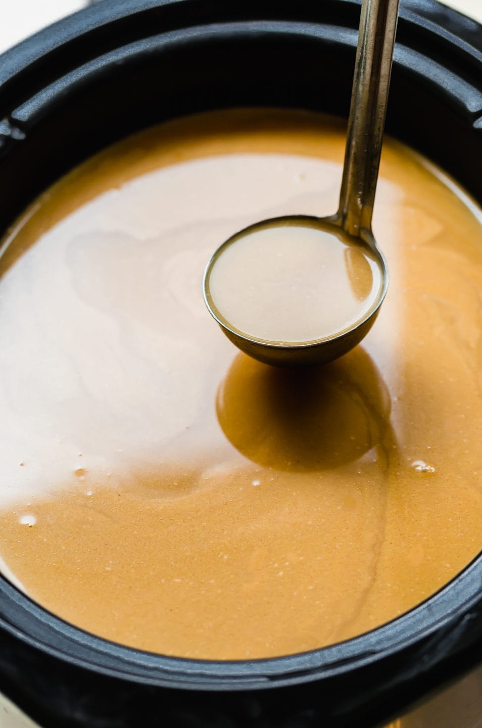 A ladle scooping out salted caramel apple cider from a slow cooker.