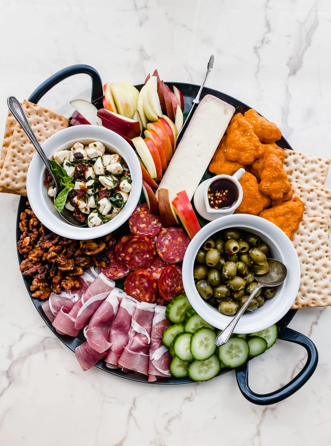 A black iron tray filled with cheese, vegetables and charcuterie. 