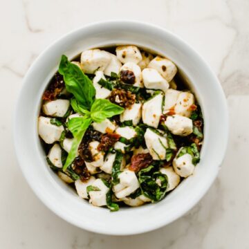A white bowl filled with Italian marinated mozzarella pearls with a sprig of fresh basil on top.