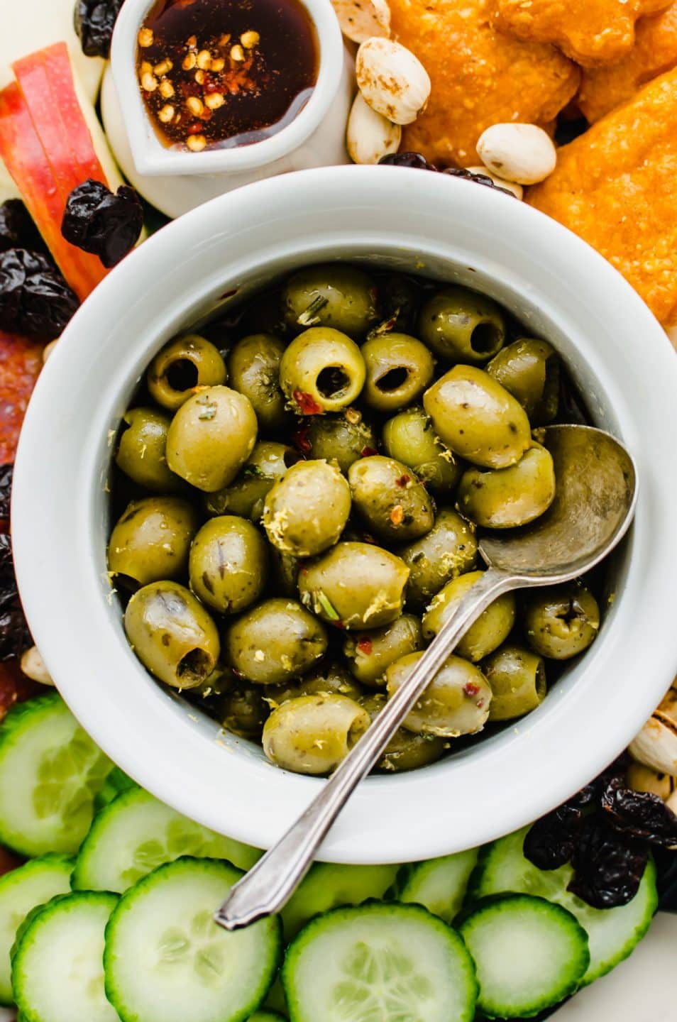 A close-up shot of a bowl of warm olives with lemon and rosemary on a cheese board. 