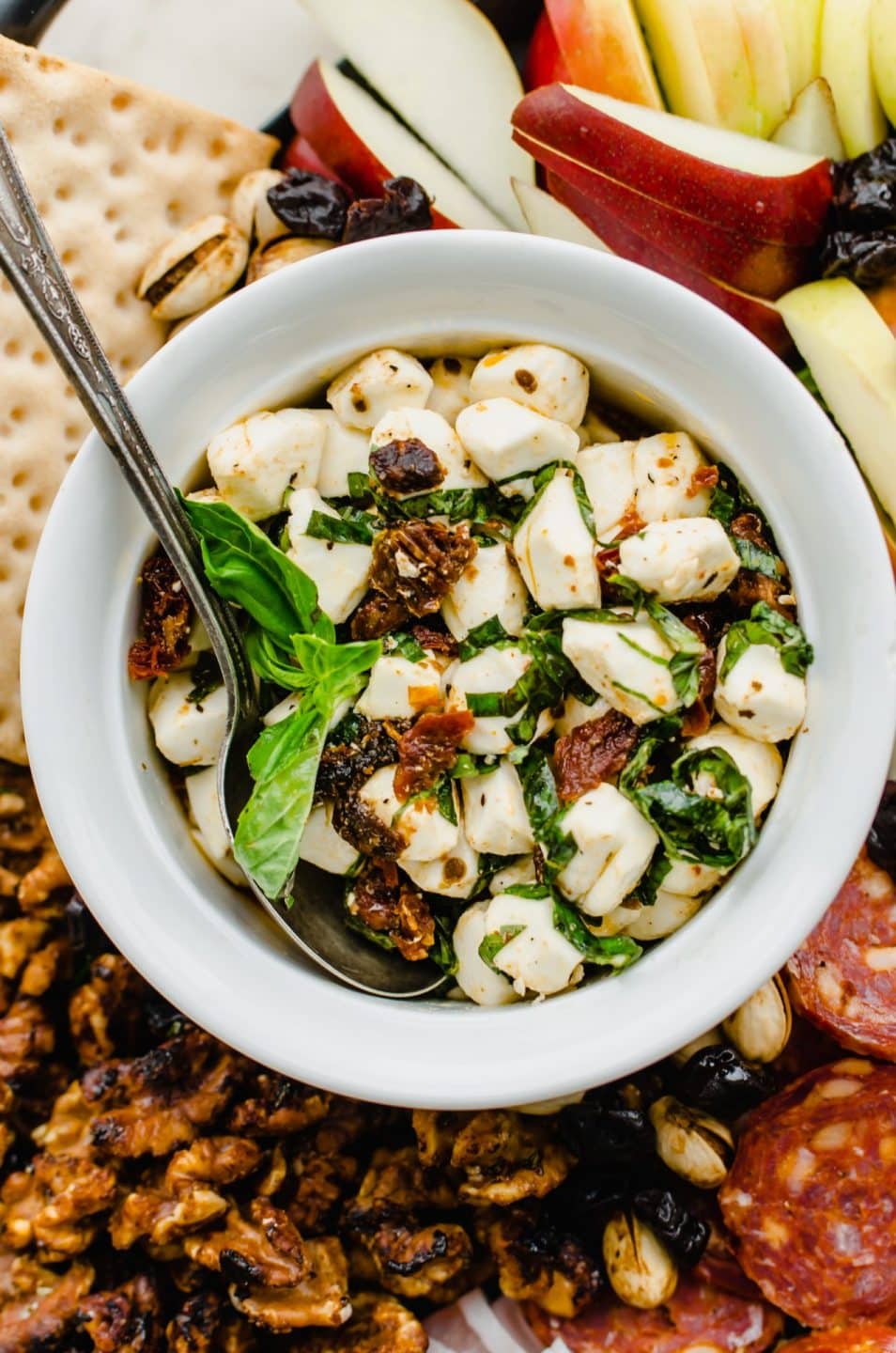 A white bowl filled with Italian marinated mozzarella pearls with a sprig of fresh basil on top.