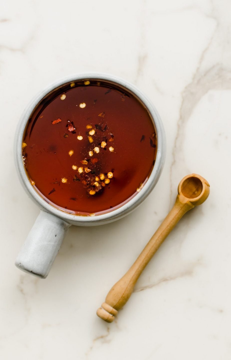 A small crock with a handle filled with hot honey drizzle and a wooden scoop on the side.