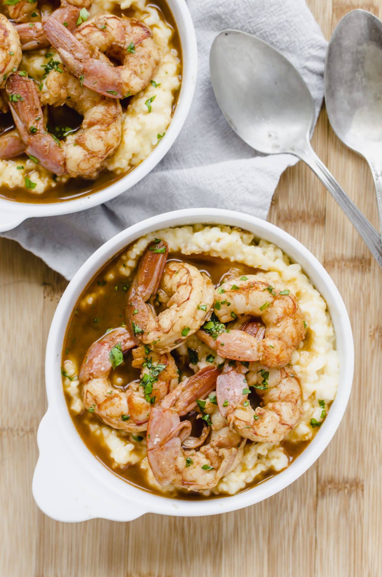 A close up shot of a white bowl filled with barbecue shrimp and grits with an antique spoon on the side. 