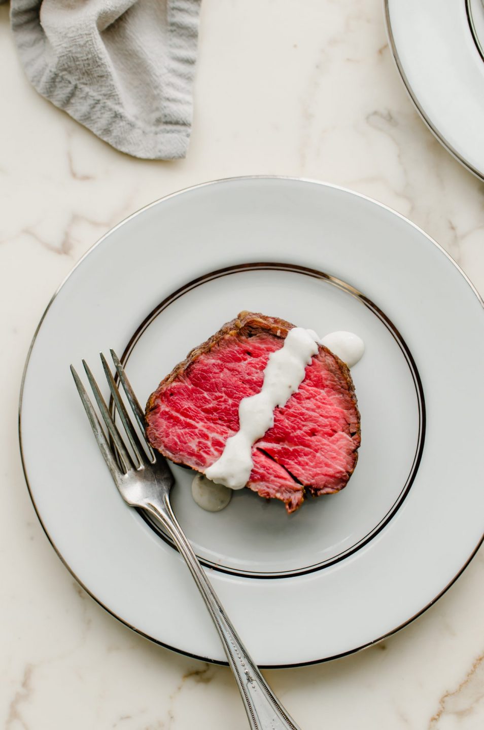 A slice of beef tenderloin on a china plate with horseradish sauce on top.