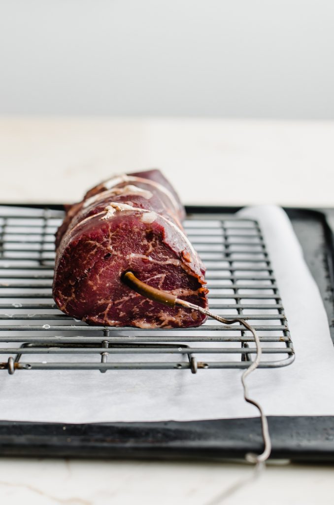 A roasted beef tenderloin with a thermometer inserted into the center.
