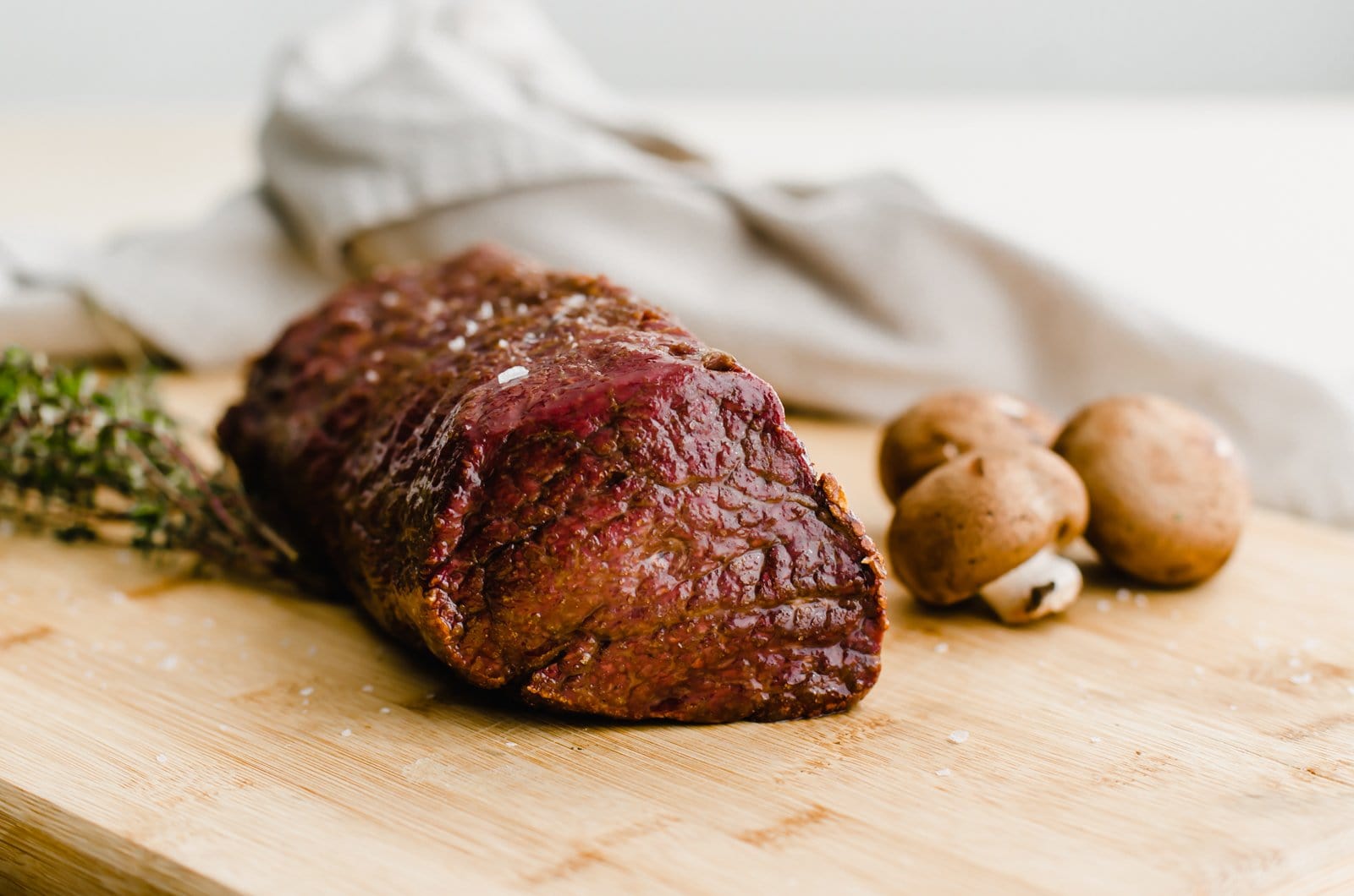 A close up of a roasted beef tenderloin on a cutting board with mushrooms on the side.
