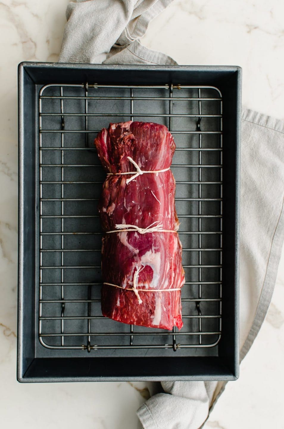 A tied beef tenderloin on a wire rack in a baking dish.