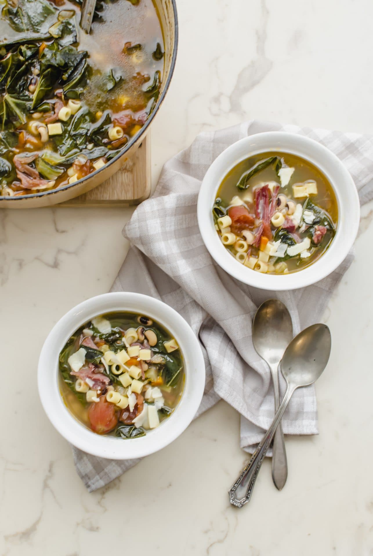 Two white bowls with pasta e Fagioli next to a yellow Dutch oven filled with soup.