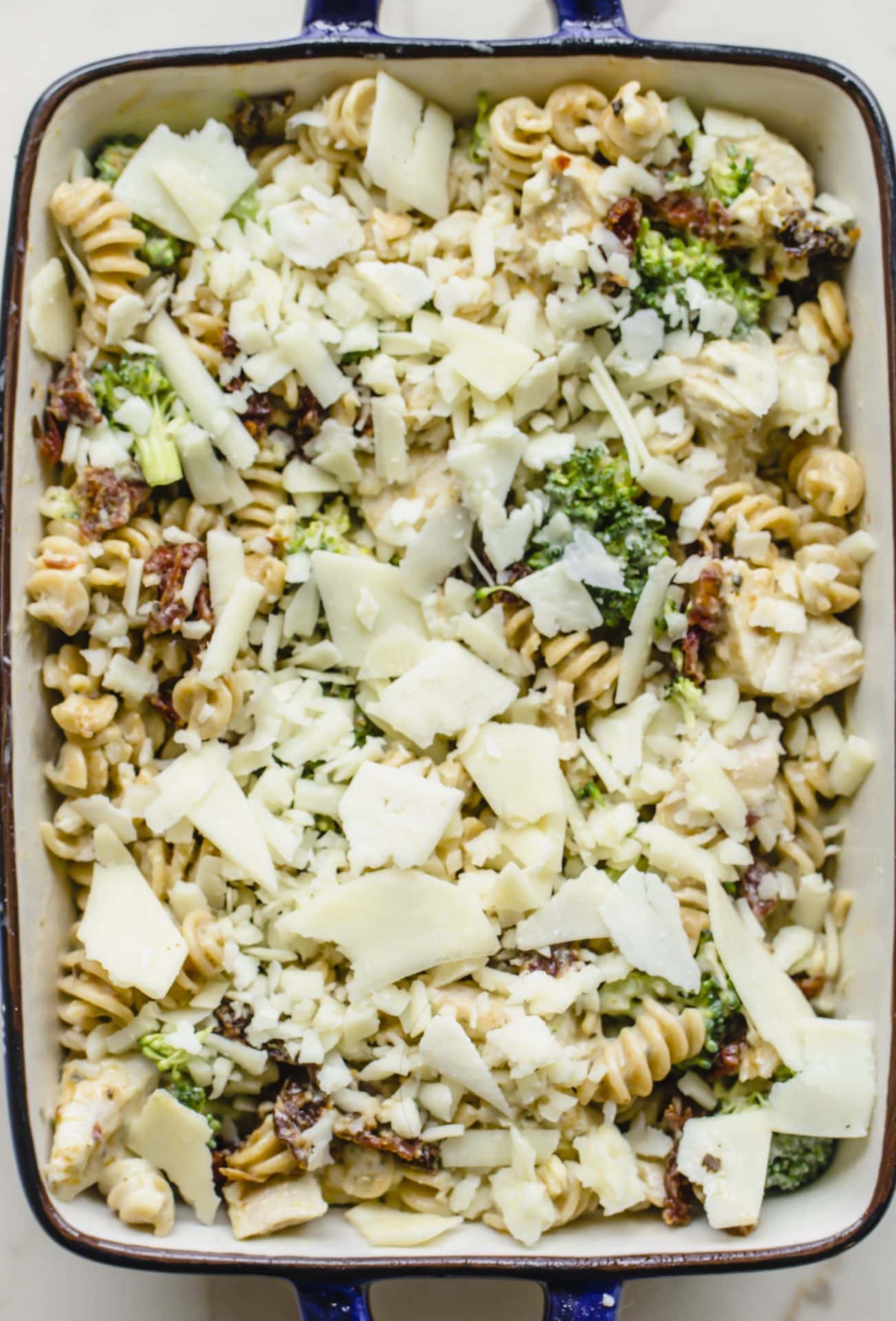 An unbaked casserole dish filled with Chicken Rotini Bake and topped with cheese.