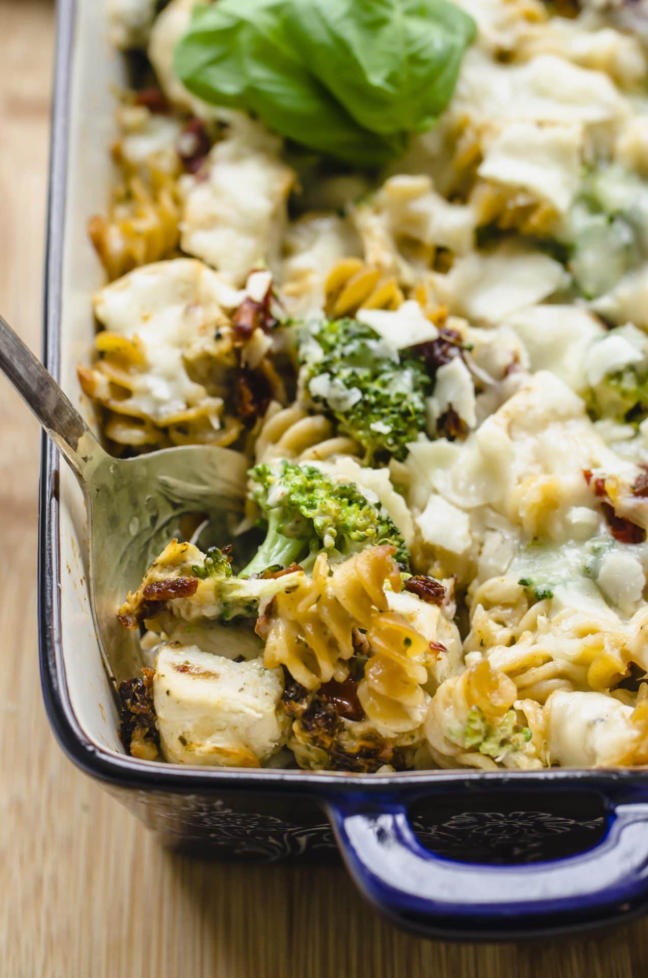 A serving spoon lifting up a serving of Chicken Rotini Bake from a blue casserole dish.