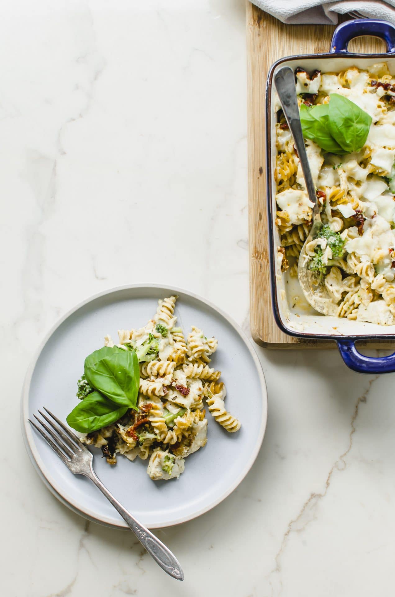 A blue plate with a serving of Chicken Rotini Bake next to the casserole dish on a cutting board.