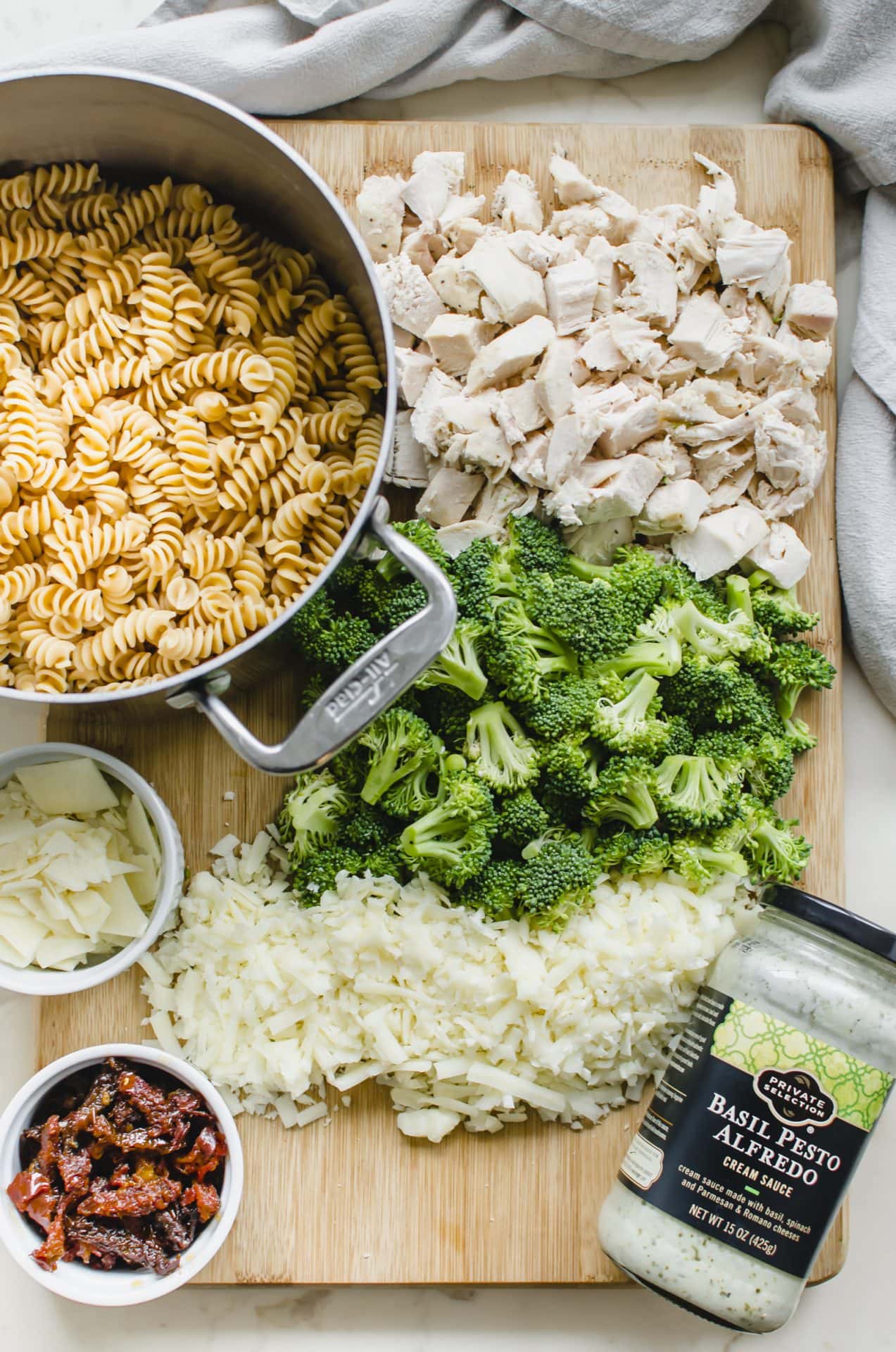 A cutting board with all of the prepped ingredients spread out for making Chicken Rotini Bake.