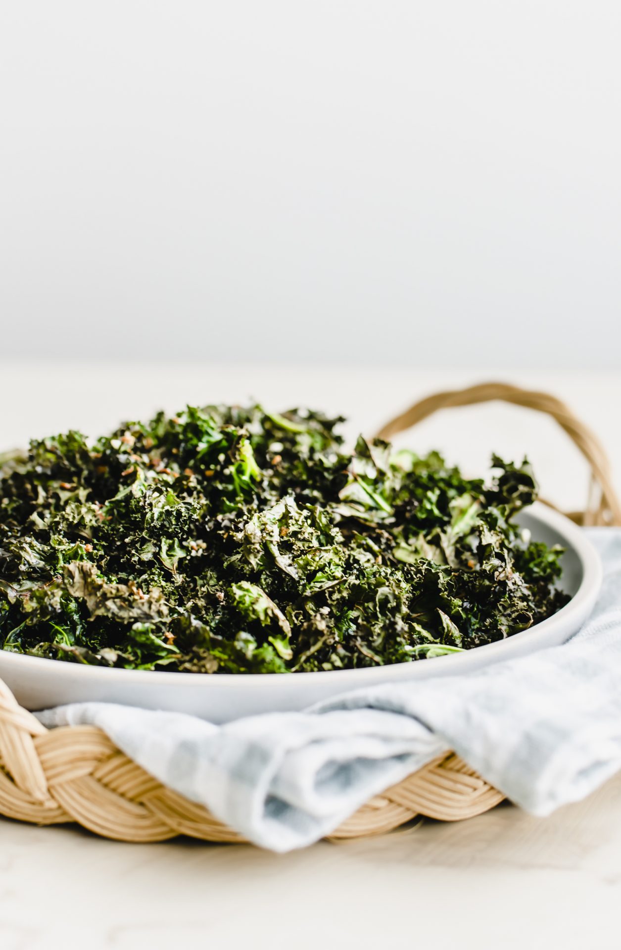 A side shot of a plate of kale chips on a gingham dish towel inside a rattan charger.