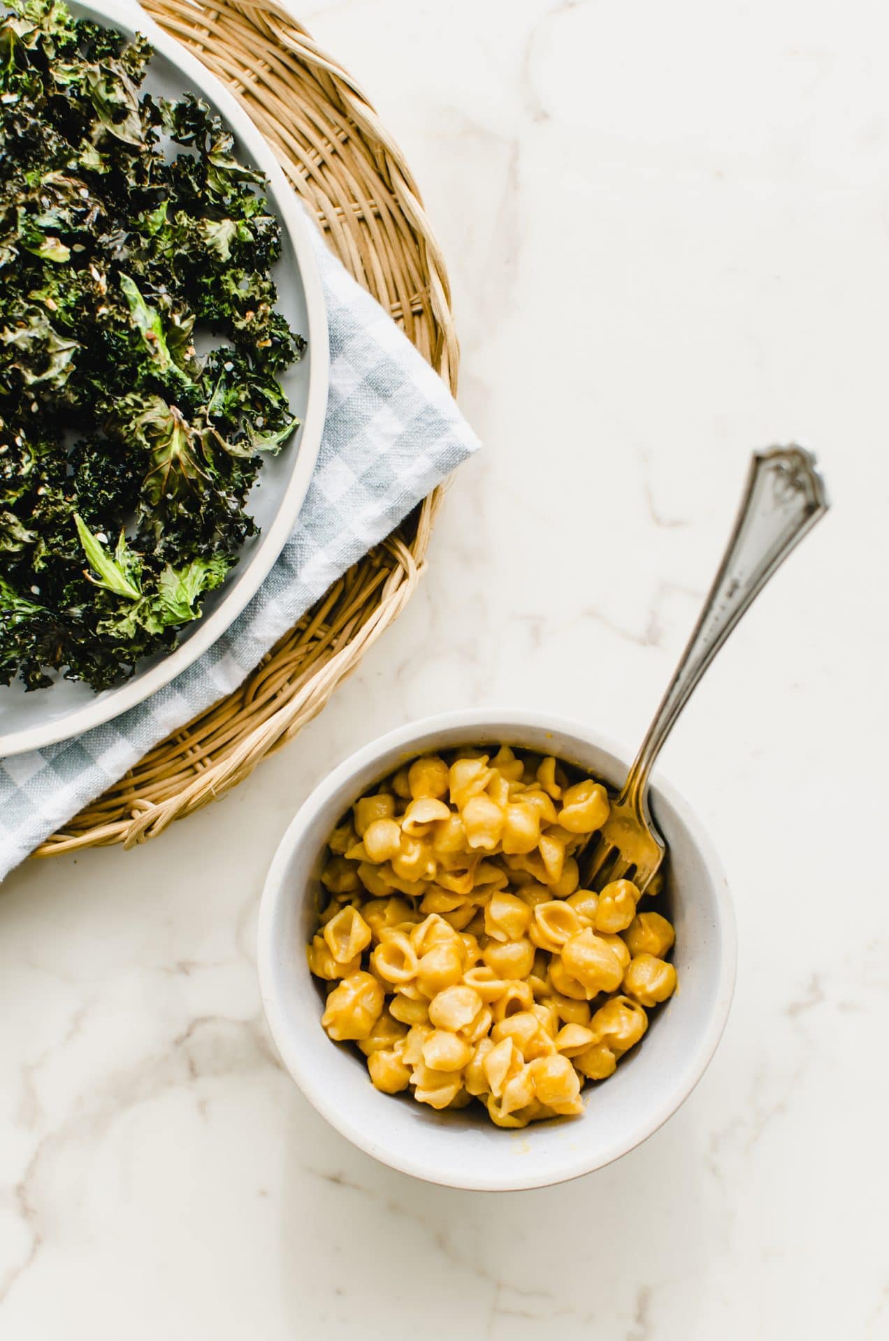 A bowl of mac and cheese with a plate of kale chips on the side.