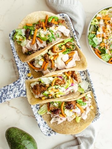 Rotisserie chicken tacos on a speckled blue tray on a white marble counter.
