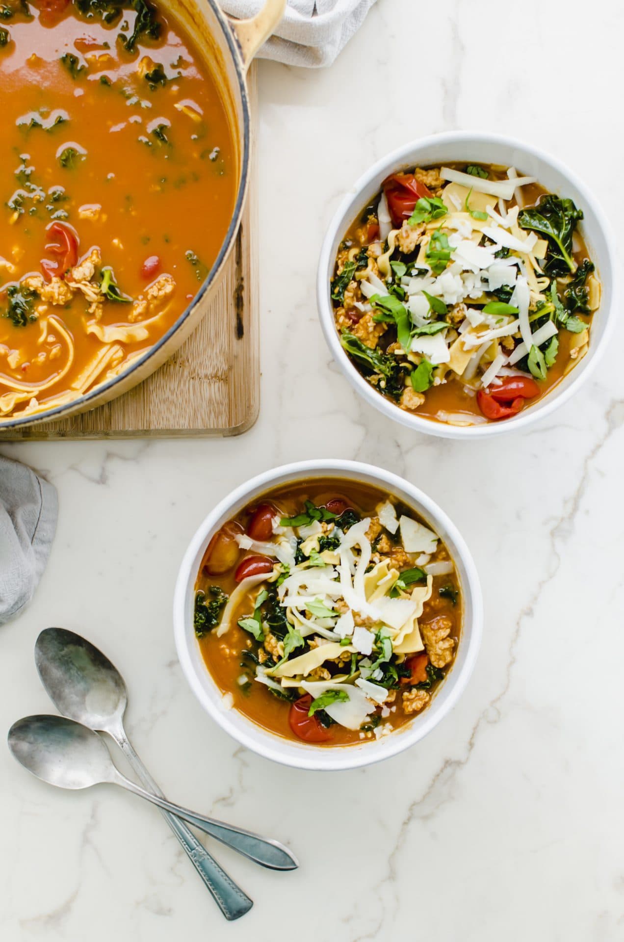 Two white bowls filled with Lasagna Soup next to a Dutch oven of lasagna soup on a white counter top. 