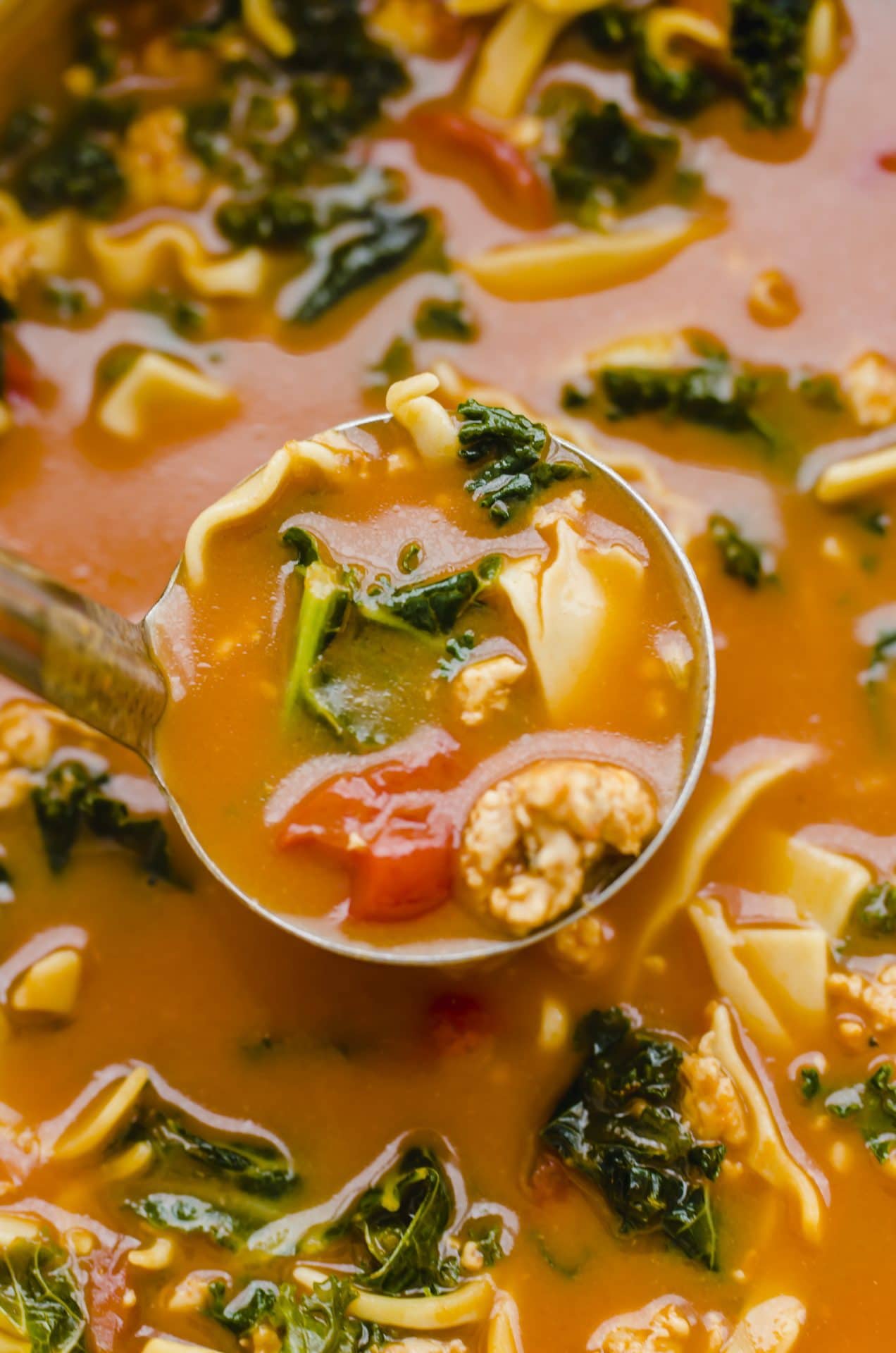 A ladle lifting out lasagna soup from a Dutch oven. 