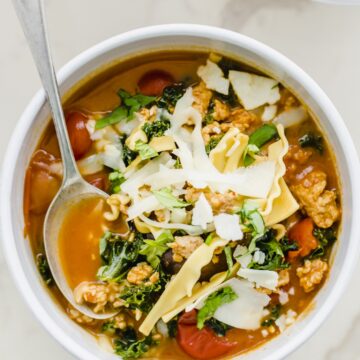 A white bowl filled with lasagna soup and topped with cheese and a spoon in the bowl.