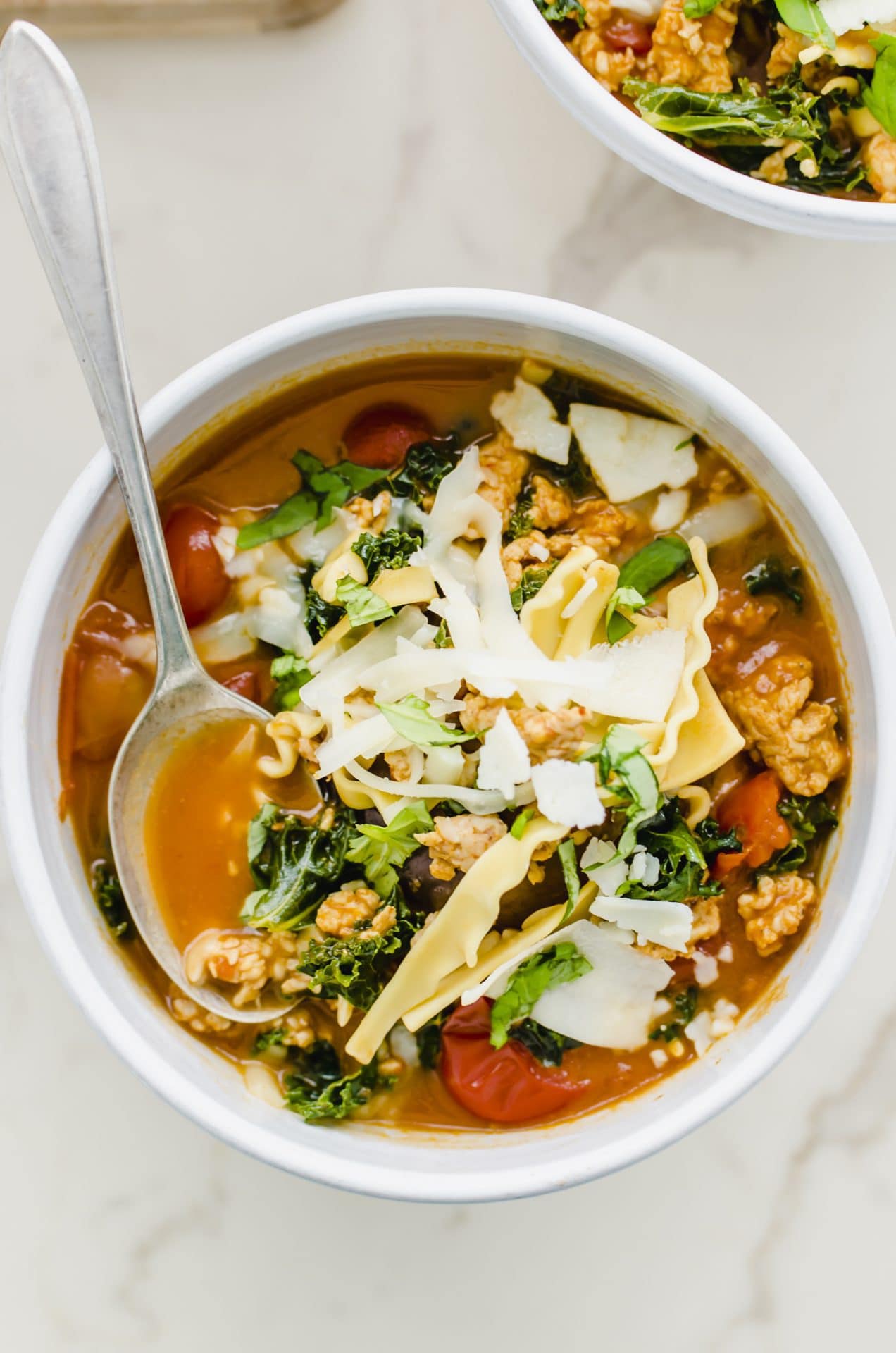 A white bowl filled with lasagna soup and topped with cheese and a spoon in the bowl. 