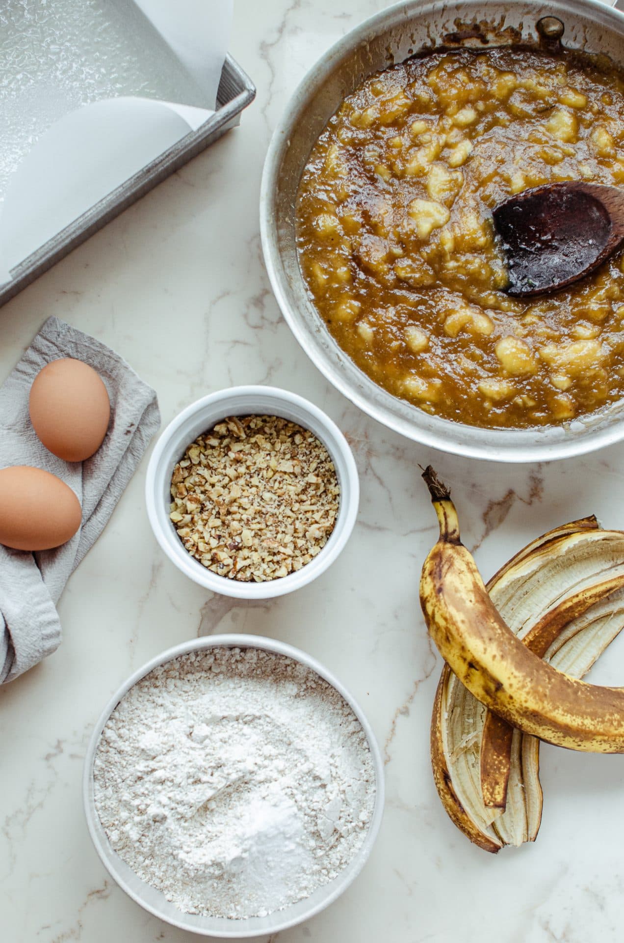 Measured ingredients in white bowls on a marble counter top for prepping banana bread. 