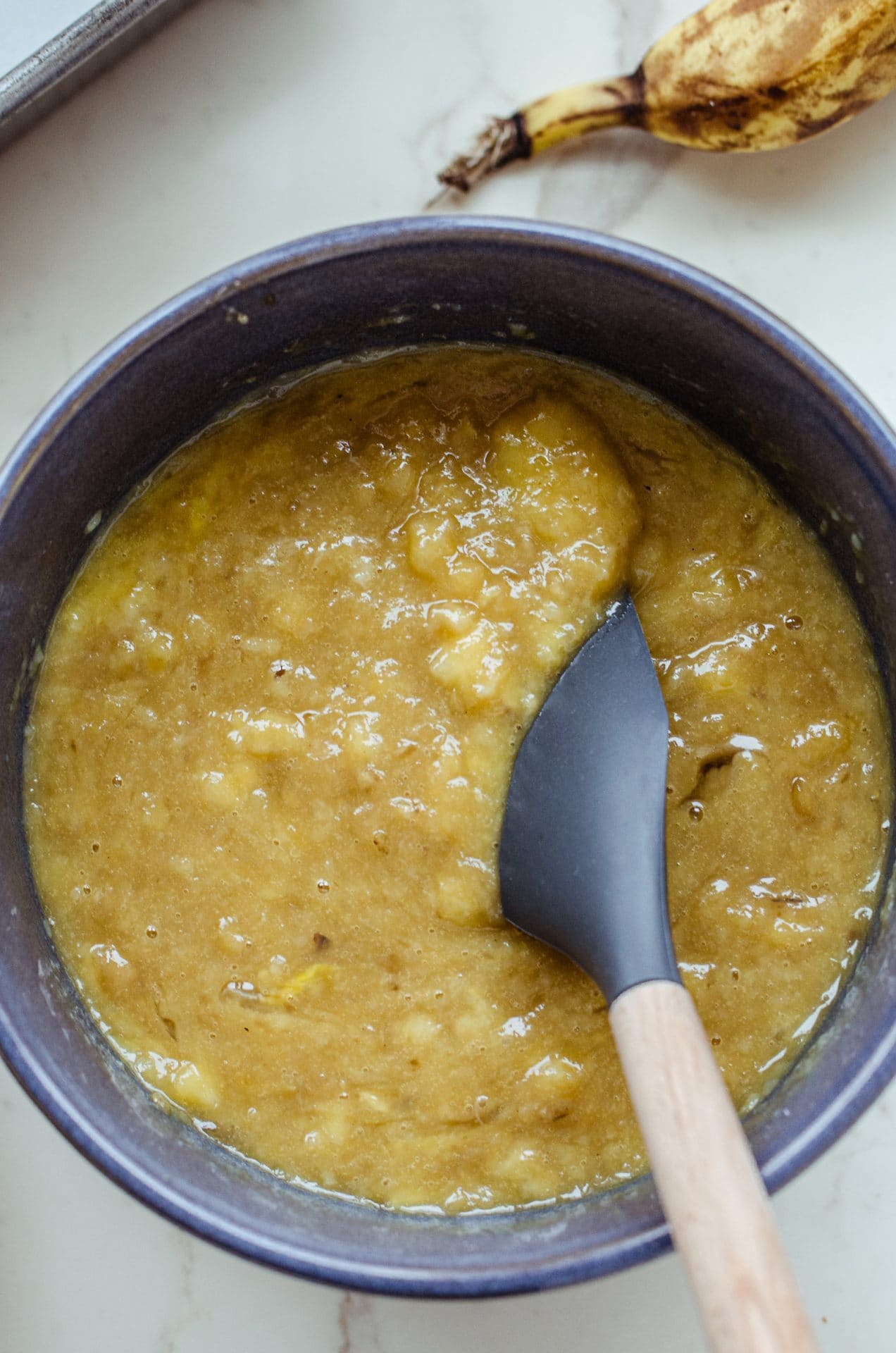 A gray rubber spatula mixing banana bread batter in a blue bowl. 