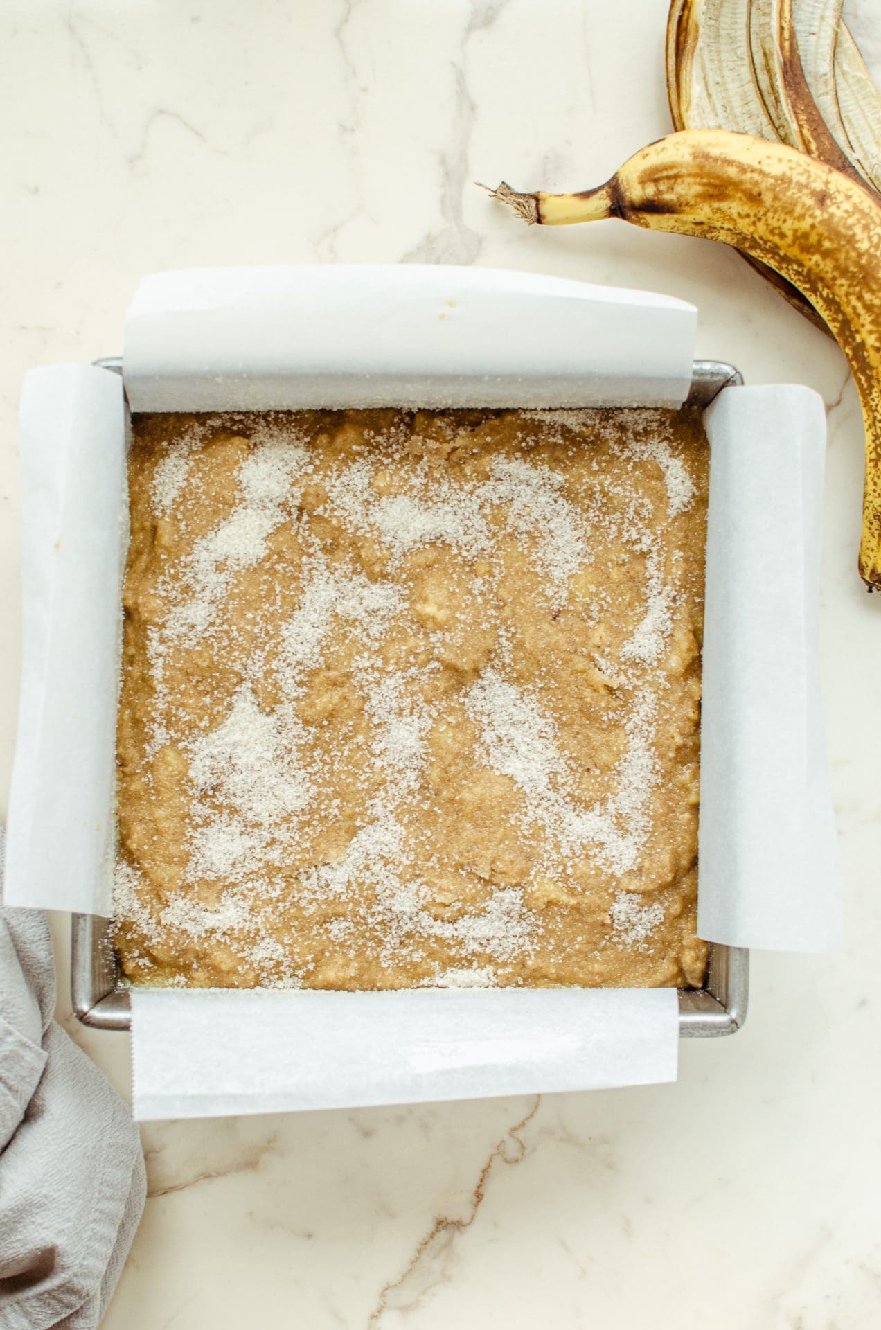 Unbaked banana bread batter in a square cake pan sprinkled with sugar on top. 