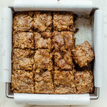 A square pan lined with parchment paper and filled with sliced squares of banana bread.