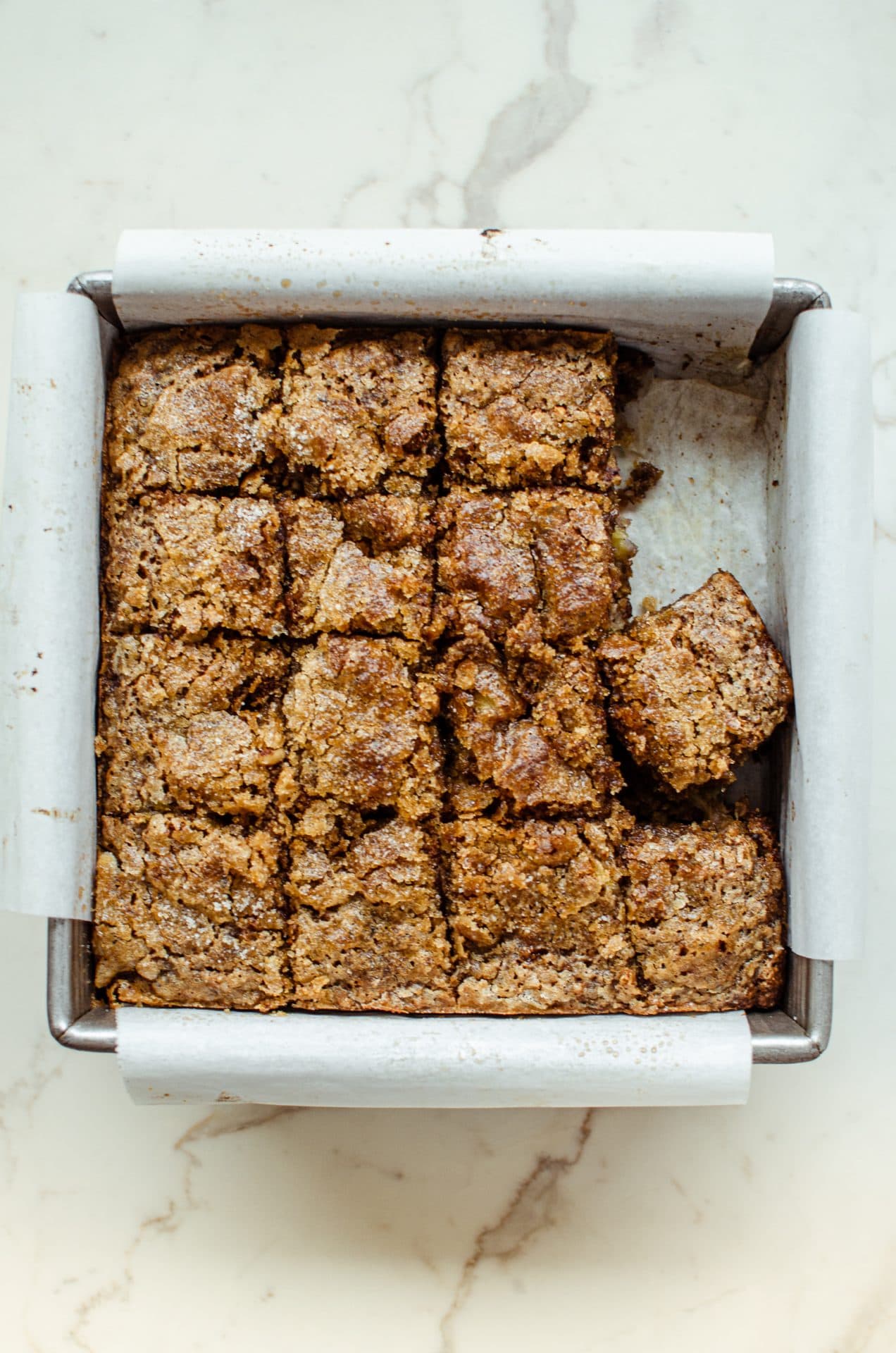 A square pan lined with parchment paper and filled with sliced squares of banana bread. 