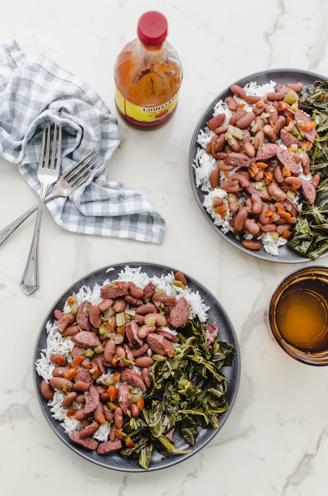 Two grey plates with red beans and rice on a white counter with a gold tumbler on the side.