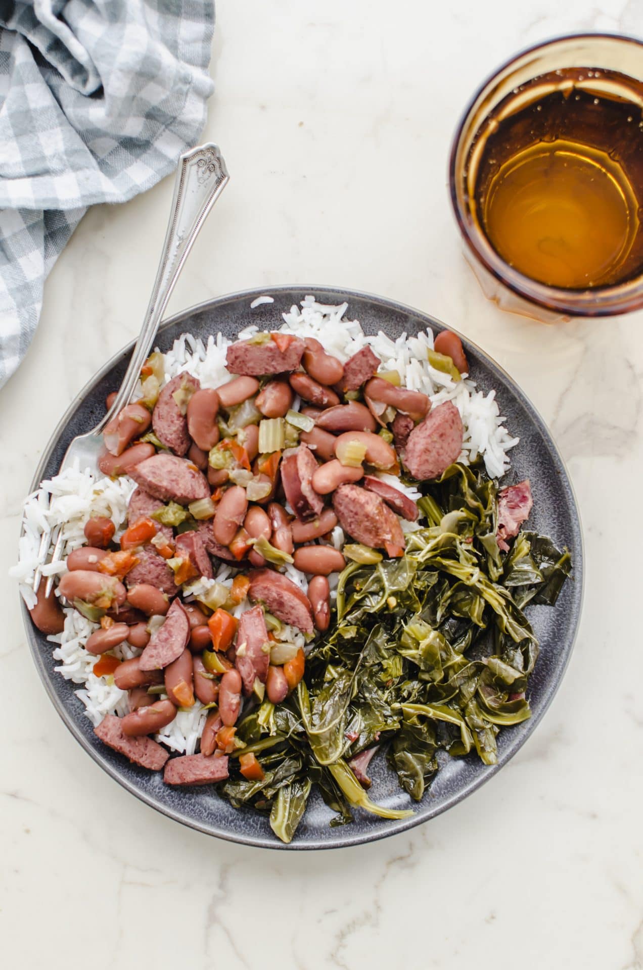 A gray plate of red beans and rice with a gingham dish towel and a glass of water on the side.