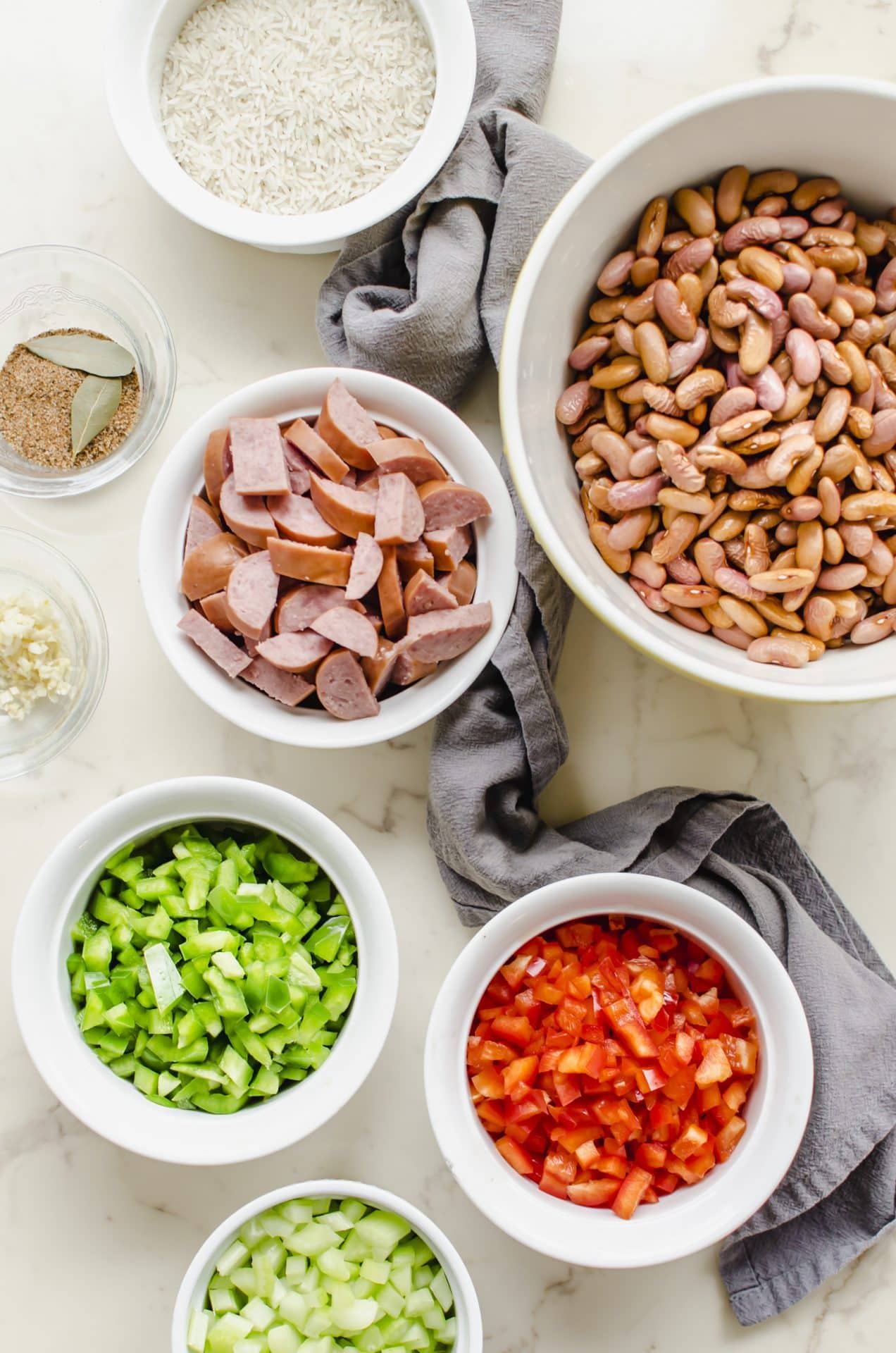 An overhead shot of white bowls with all of the prepped ingredients for red beans and rice.