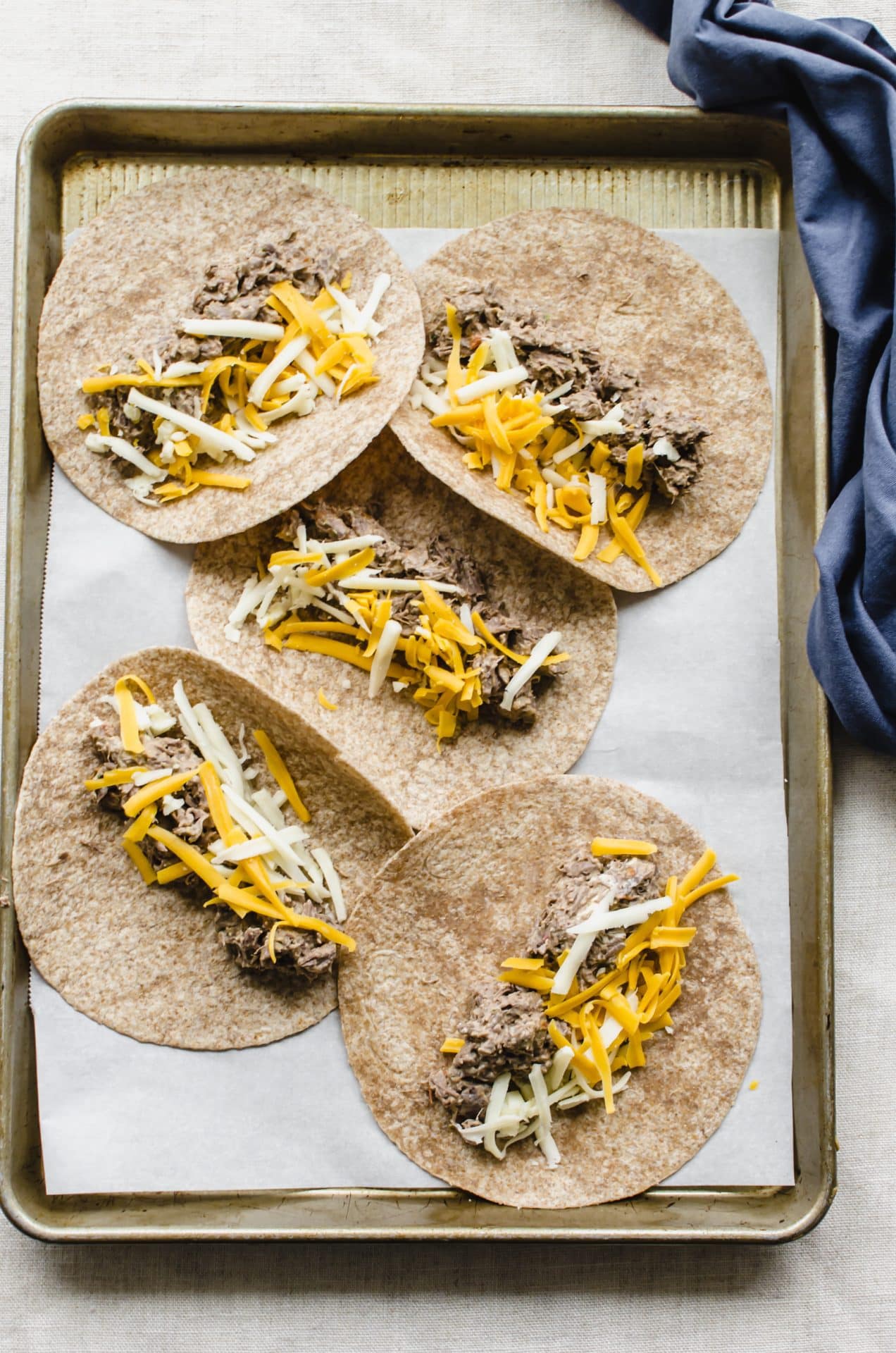 Tortillas on a sheet pan with shredded beef and cheese in the center.