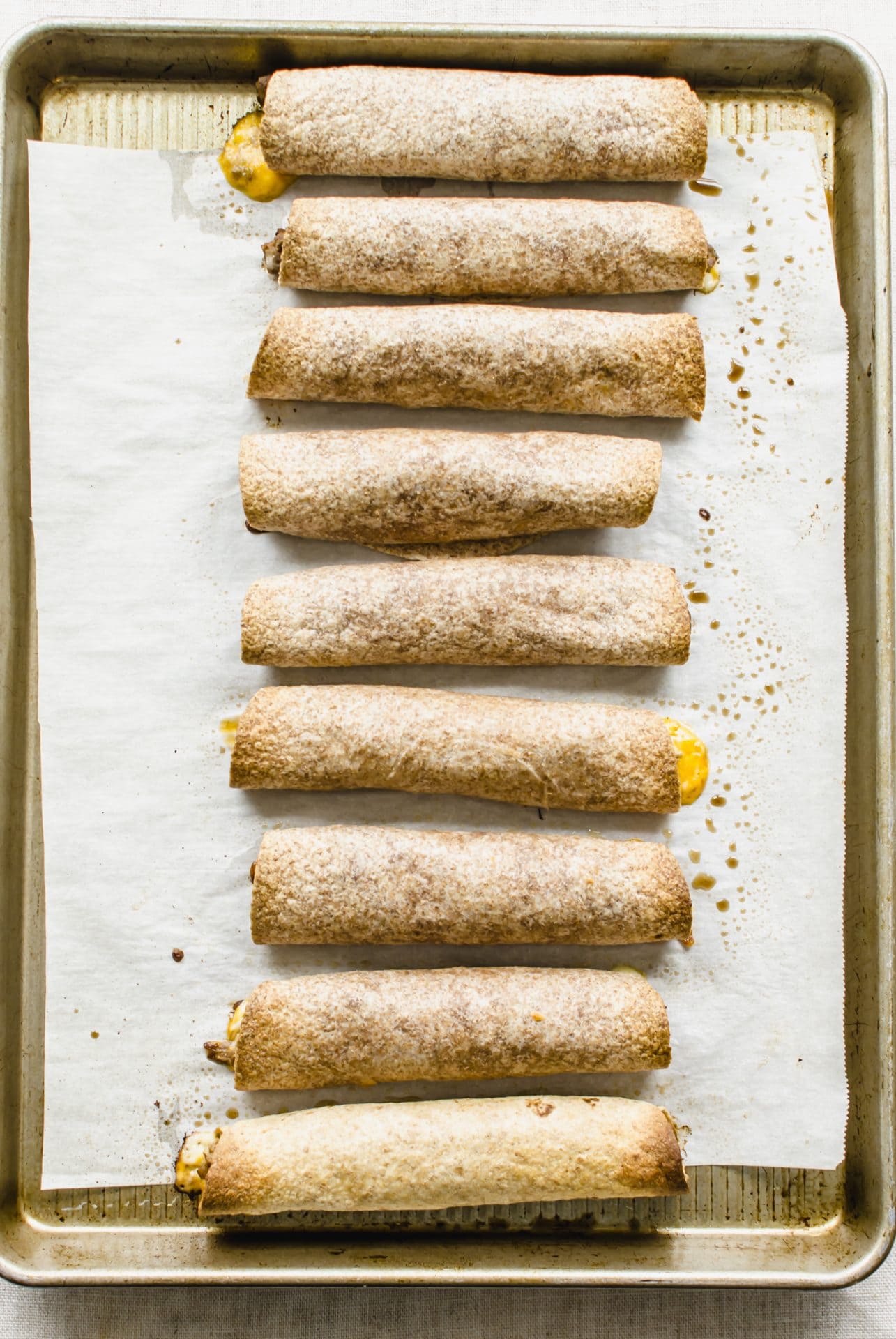 Baked beef taquitos on a sheet pan lined with parchment paper.