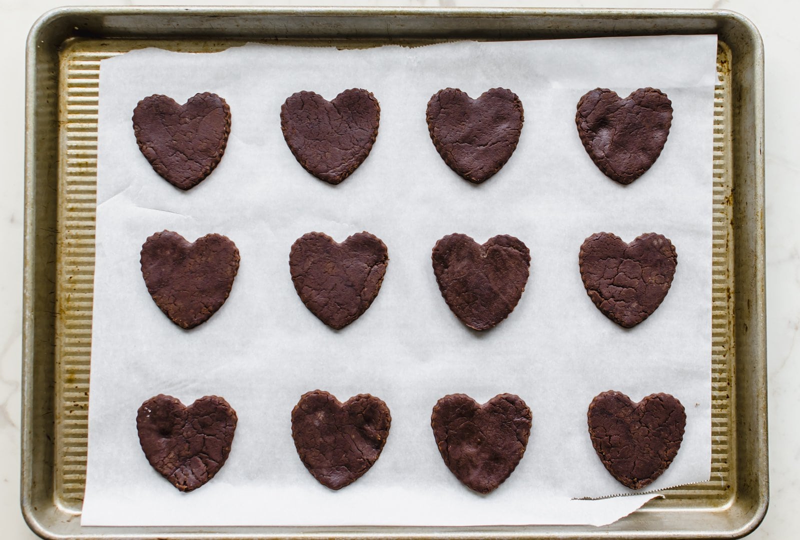 Unbaked heart-shaped chocolate cookies on a baking sheet with parchment paper.