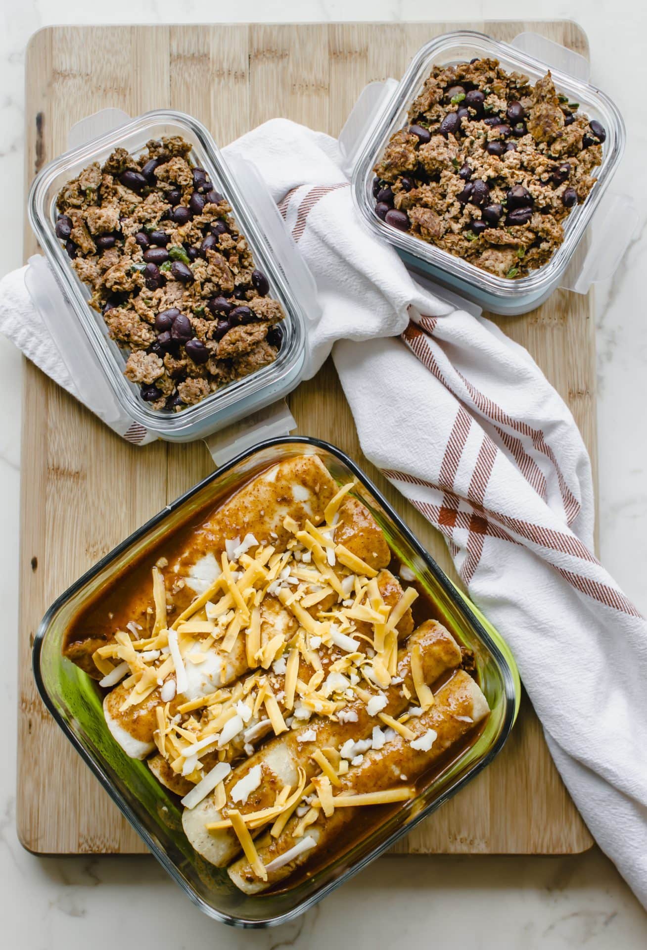 A freezer container filled with enchiladas and two meal prep containers with enchilada filling.