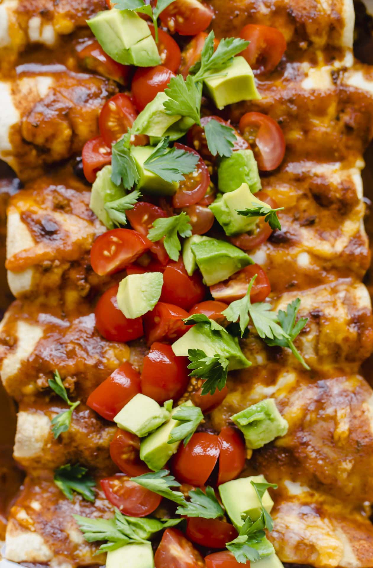 A close up shot of baked enchiladas topped with avocado and tomato slices.
