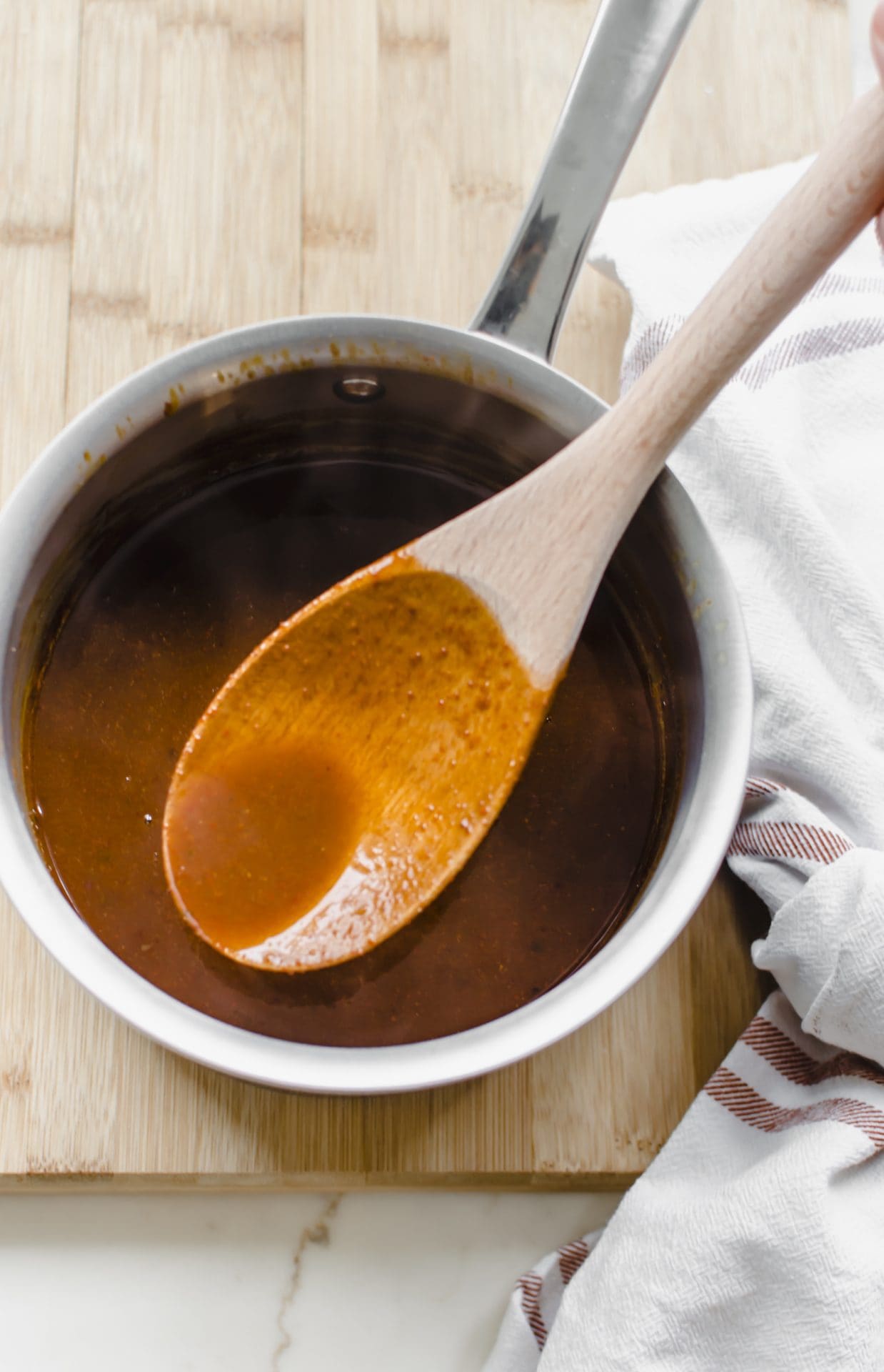 A saucepan with red enchilada sauce and a wooden spoon lifting some out.