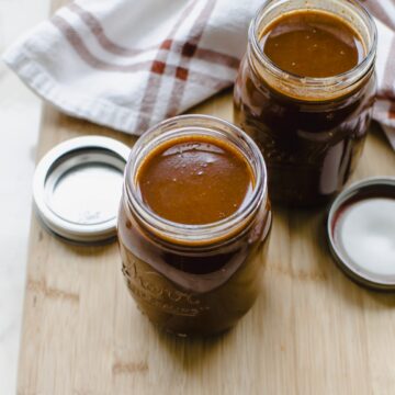 Two mason jars filled with red enchilada sauce on a wooden cutting board.