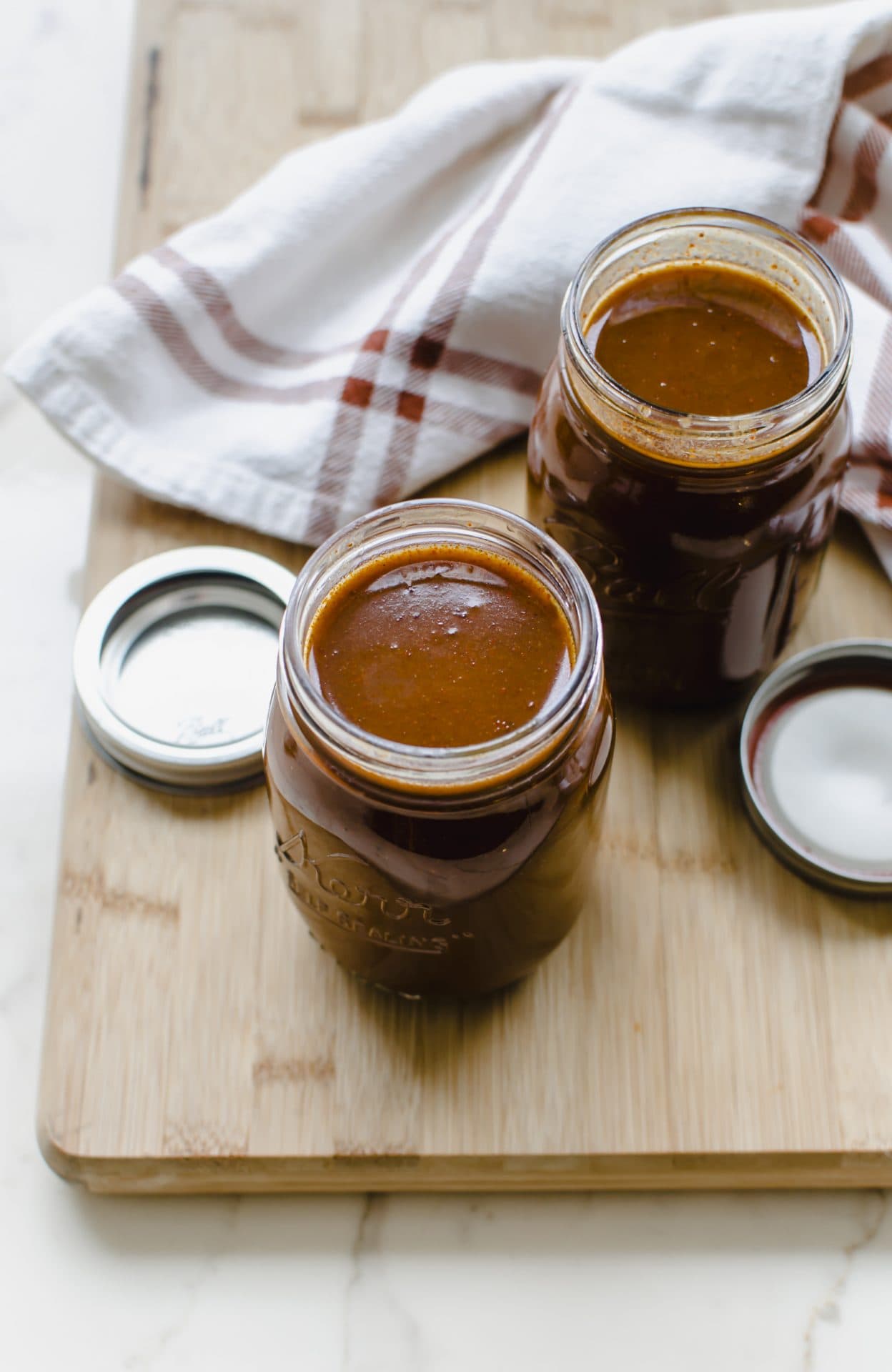 Two mason jars filled with red enchilada sauce on a wooden cutting board.