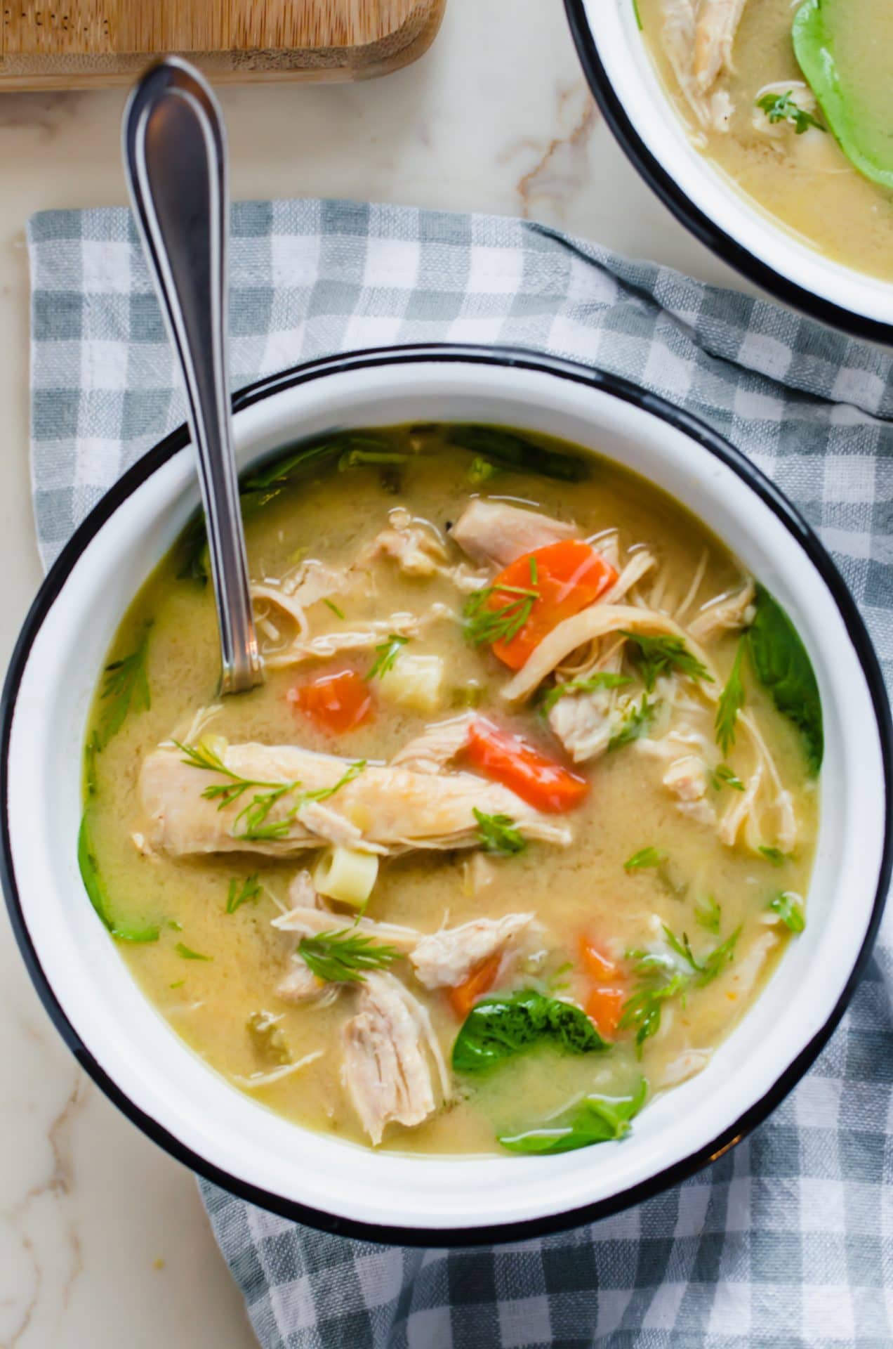 A close-up shot of a white enamel bowl filled with lemon chicken noodle soup.