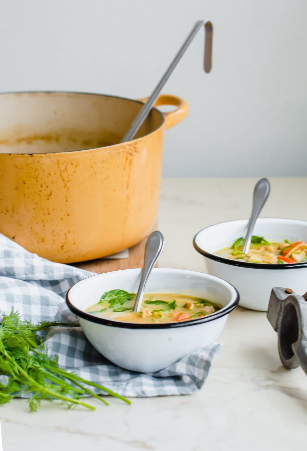 Two white enamel bowls filled with lemon chicken soup next to a pot of soup on the side.