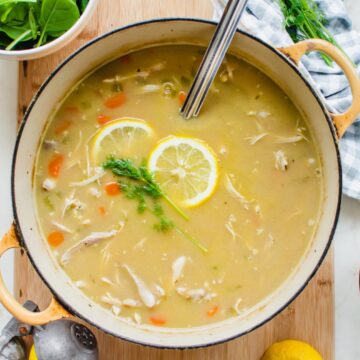 A yellow Dutch oven filled with lemony chicken and orzo soup with a ladle and lemons on the side.
