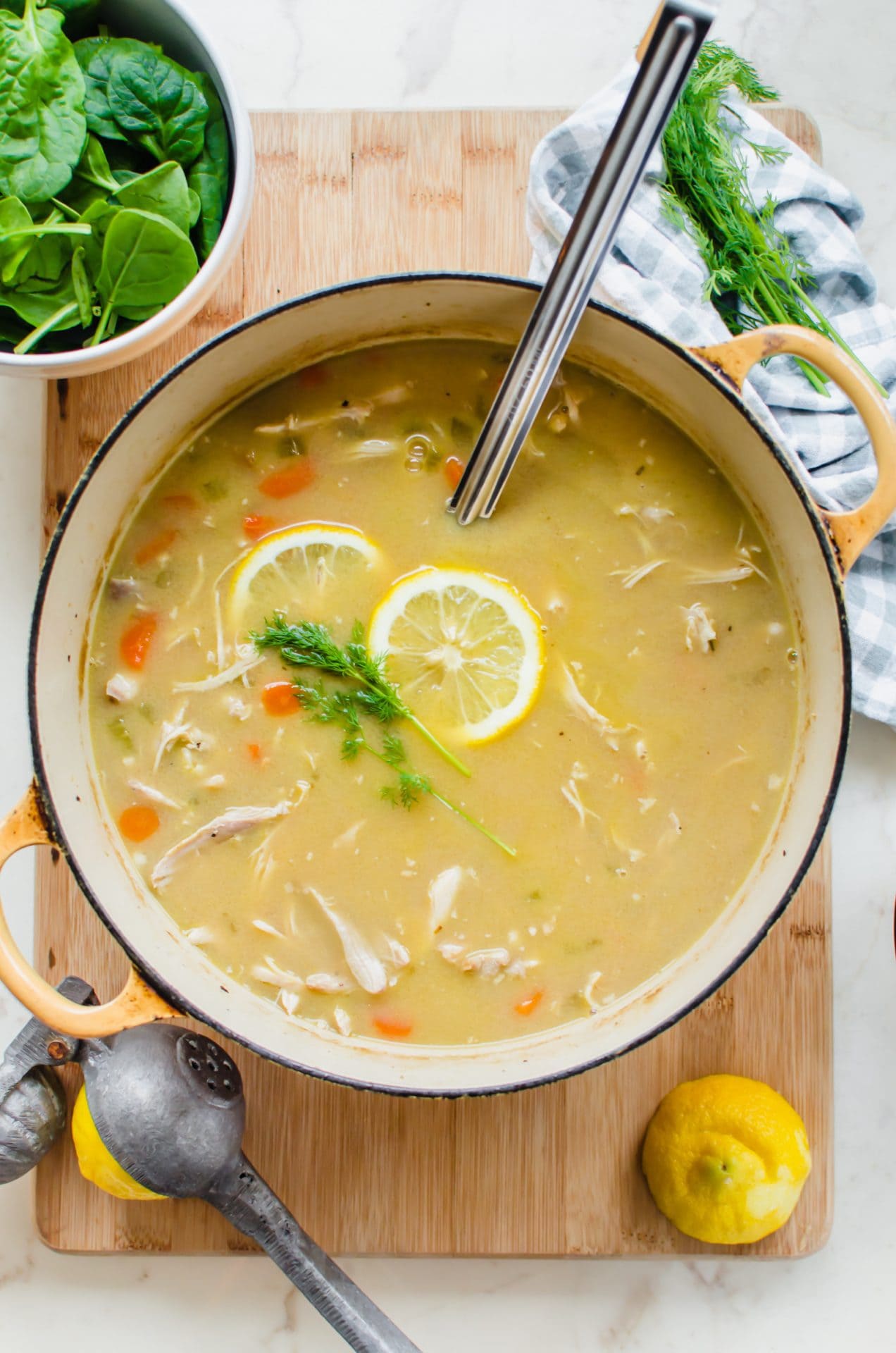 A yellow Dutch oven filled with lemony chicken and orzo soup with a ladle and lemons on the side.