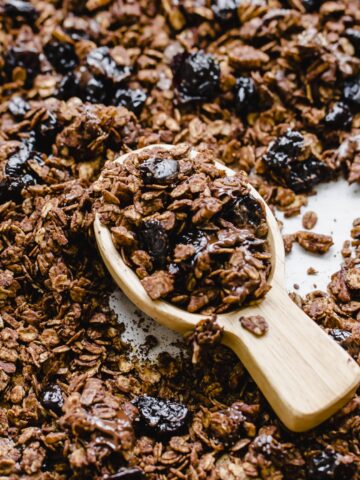 A wooden scoop filled with chocolate granola on a pan of granola.