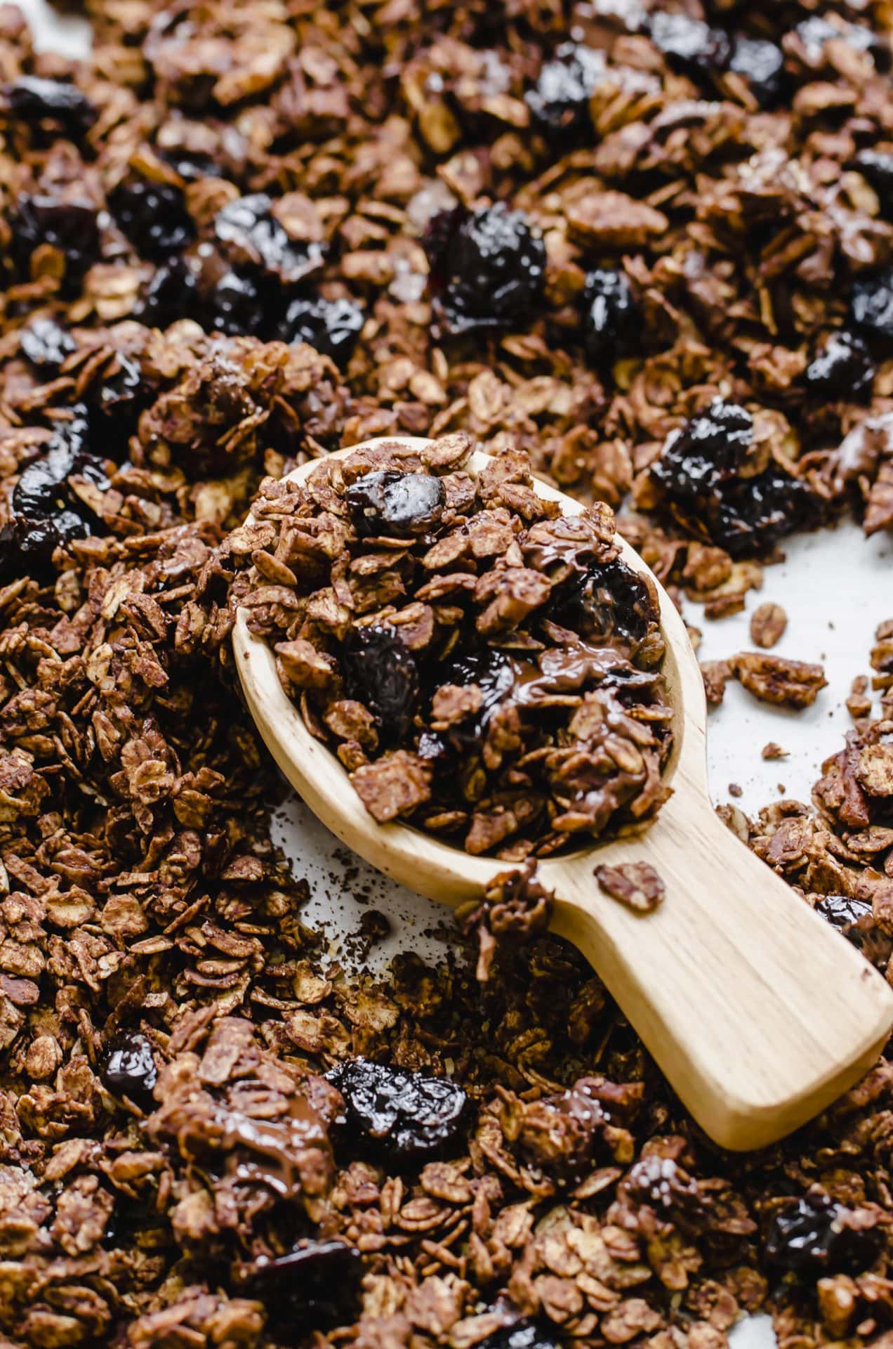 A wooden scoop filled with chocolate granola on a pan of granola.