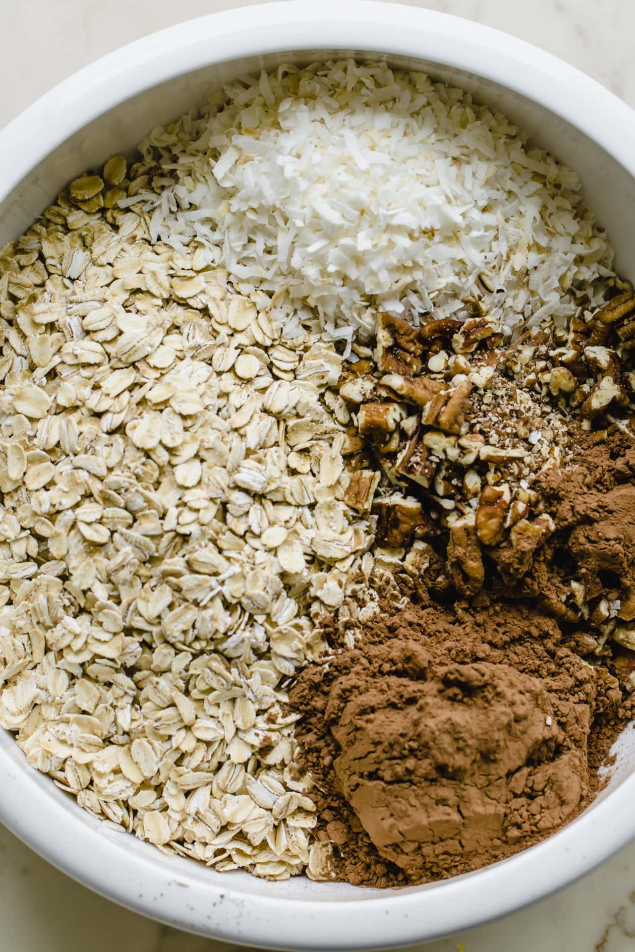 A white bowl with oats, coconut, pecans, and cocoa powder.