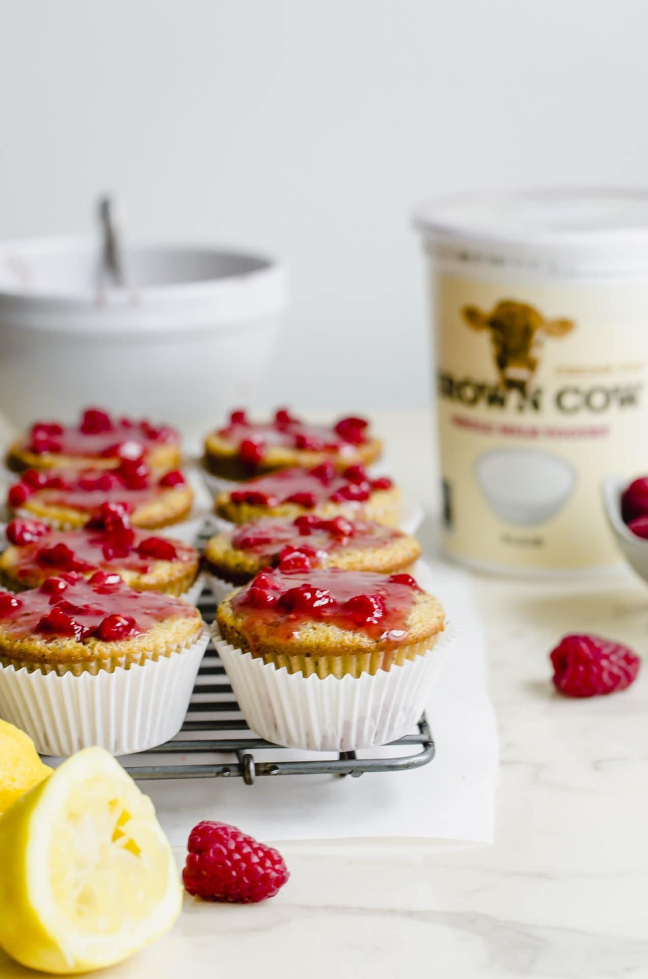 Glazed lemon poppyssed muffins on a wire rack with a container of yogurt in the background.